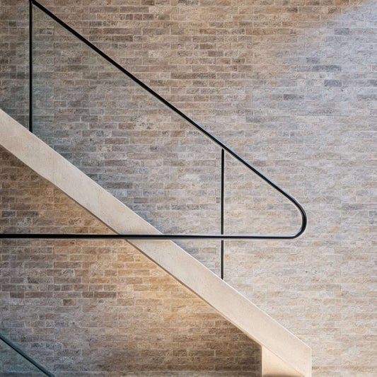 Light travertine wall with a modern staircase railing, showcasing premium natural stone and minimalist design elements.