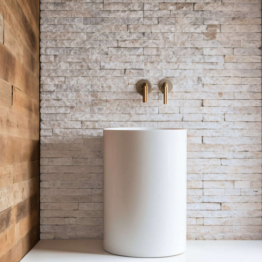 Blasted natural stone wall with polished white vessel sink, featuring minimalist design and gold faucets.