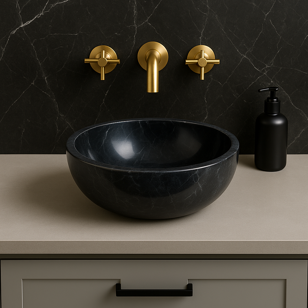Black marble vessel sink with polished finish, displayed against a dark stone wall and elegant gold faucets.