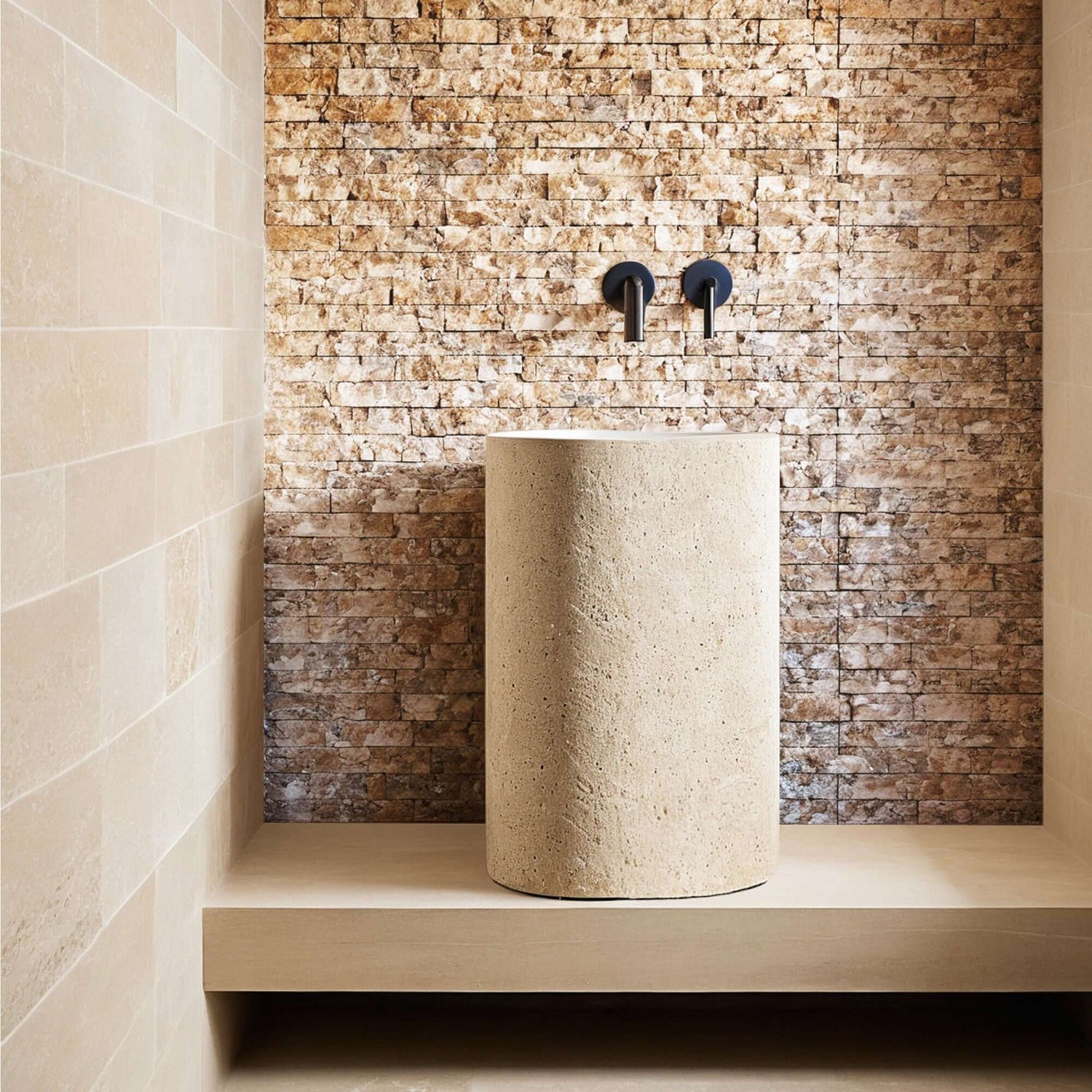 Travertine mosaic feature wall behind a stone pedestal basin