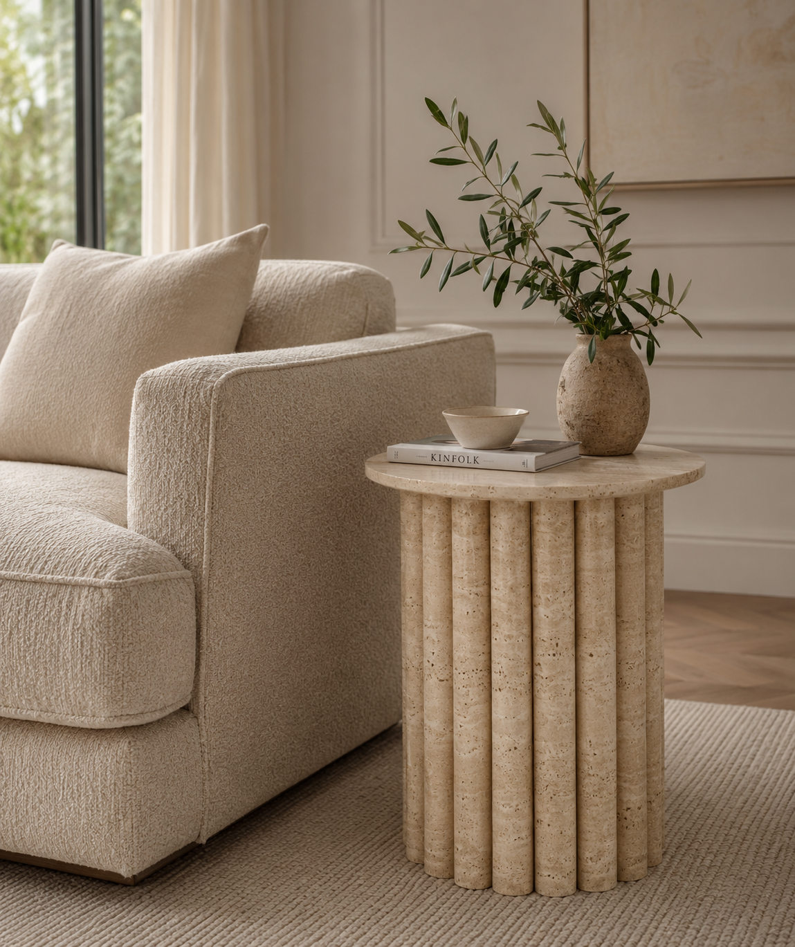 Flora Travertine Side Table styled beside a sofa in a luxury contemporary living room.
