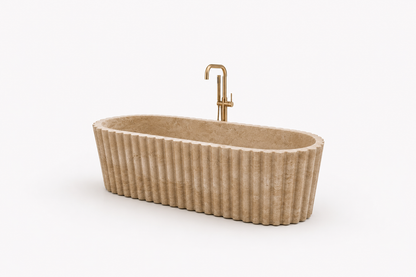 An oval freestanding bathtub in ribbed beige stone with a polished gold faucet, shown on a clean white background.